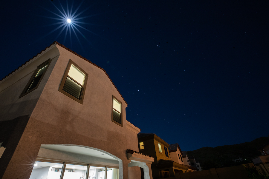 the moon and Orion over a house in phoenix arizona at night with lights on.