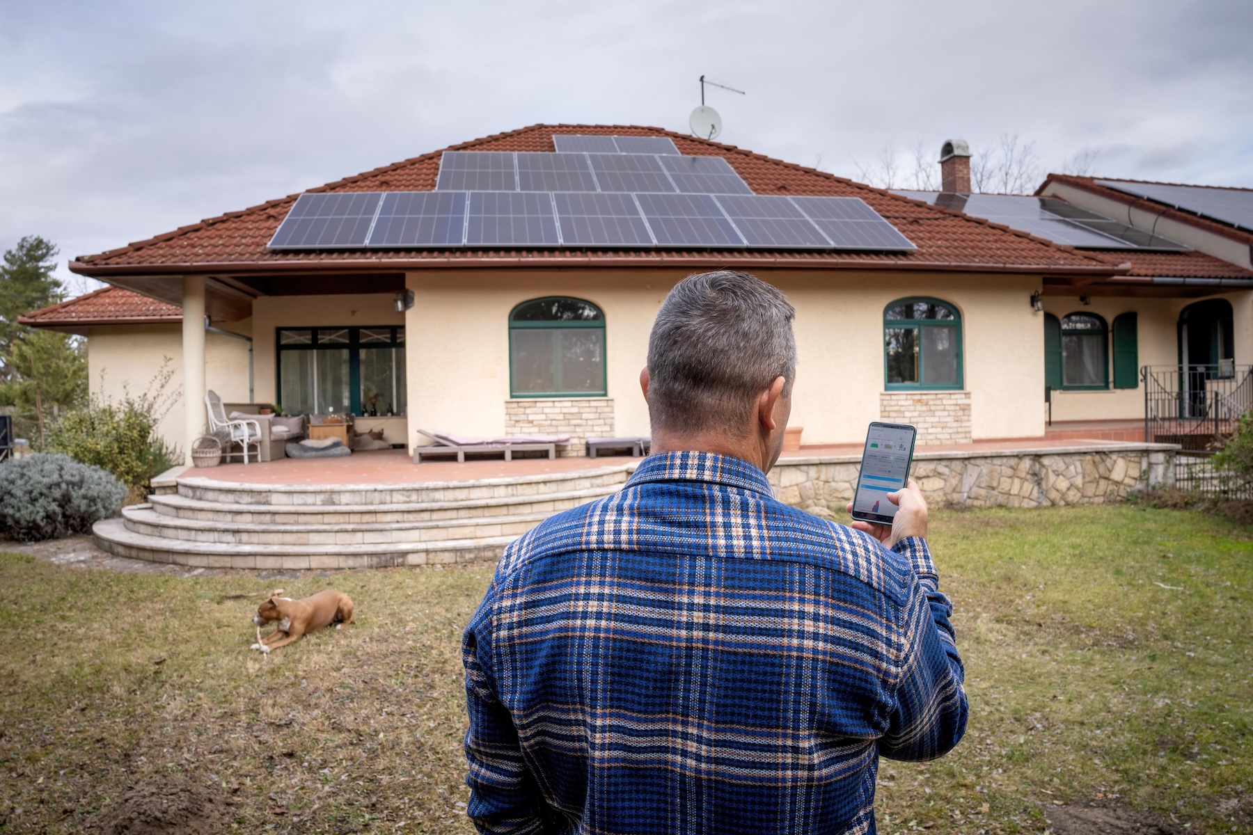 Man standing in front of house monitoring solar panel production through an app