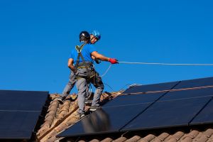 Two technicians working on photovoltaic plant on rooftop securing solar panel on sunny day